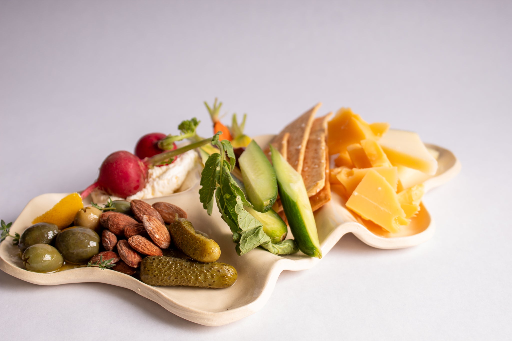 Assorted cheeses, fruits, and nuts on a white plate with a light gray background
